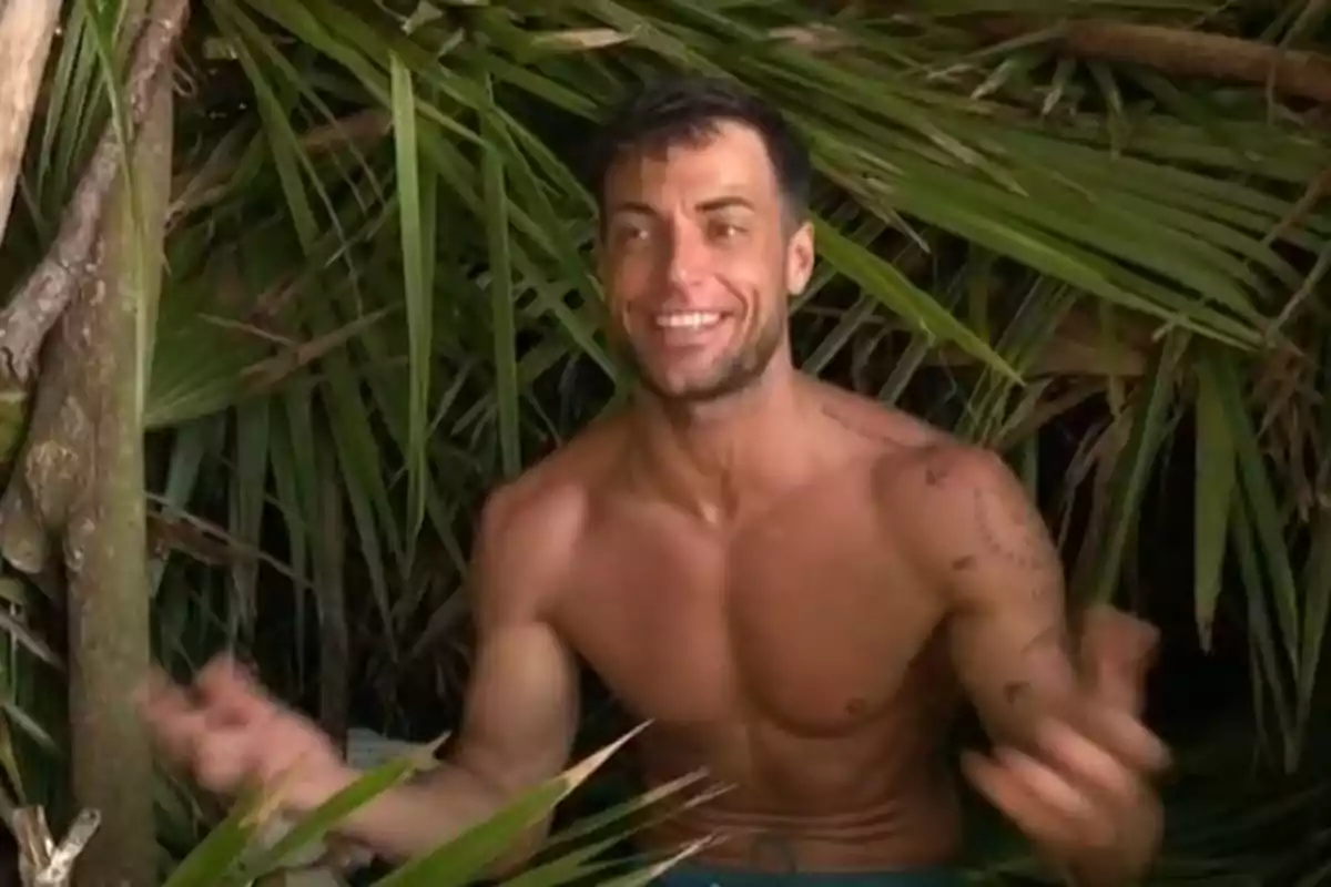 Montoya sin camisa sonríe mientras está rodeado de hojas y ramas en un entorno natural. Montoya sin camisa sonríe mientras está rodeado de hojas y ramas en un entorno natural.