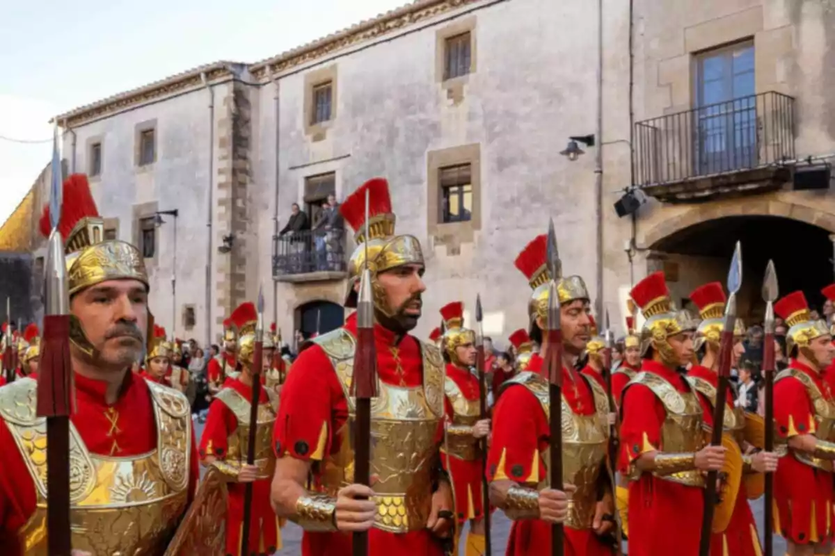 Grupo de personas vestidas como soldados romanos con armaduras doradas y túnicas rojas en una calle frente a un edificio antiguo. Grupo de personas vestidas como soldados romanos con armaduras doradas y túnicas rojas en una calle frente a un edificio antiguo.